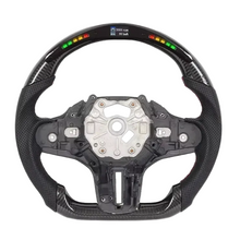 A carbon fiber racing-style steering wheel with a digital display showing battery percentage and RPM, isolated on a white background.
